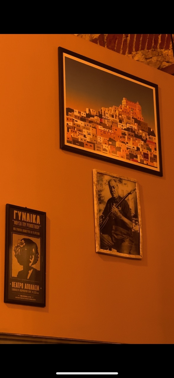 Framed pictures on the wall: Syros, a fiddler, and an Apollon Theatre poster